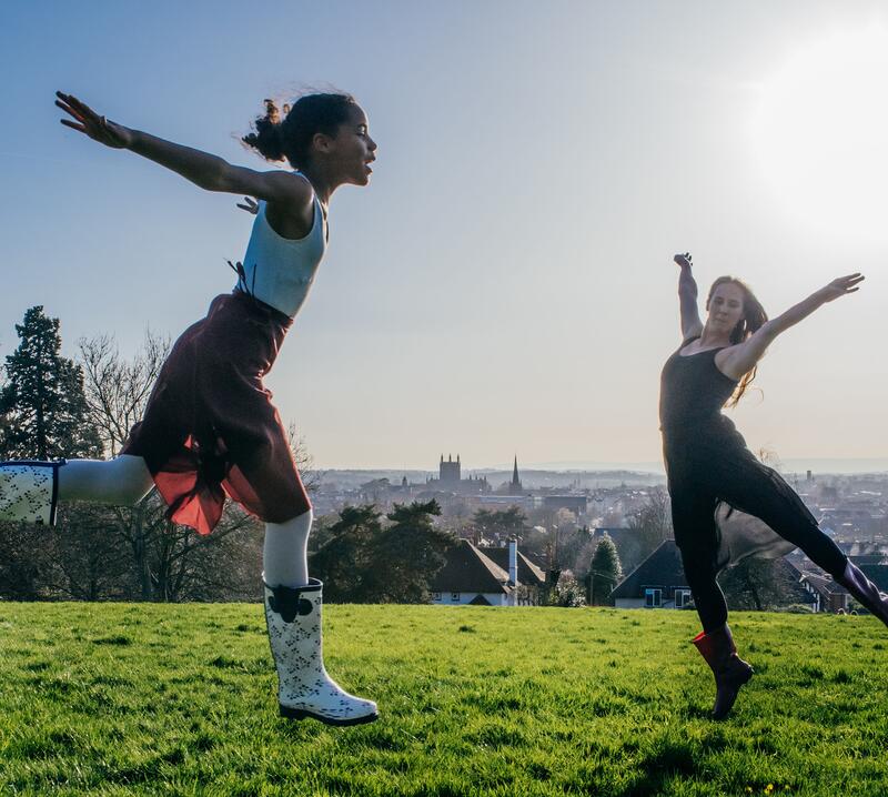 An image showing two dancers leaping in the air outside on a sunny day