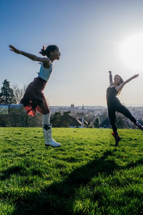 Herefordshire Cultural Partnership is leading on cultural strategy in the county and wants to engage more people. Photo by Toni Ward. An image showing two dancers leaping in the air. They are outside on grass, and the sun is shining brightly.