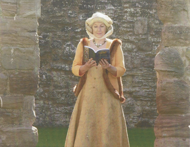 Image of a woman in medieval dress reading a book and standing in the surrounds of a castle
