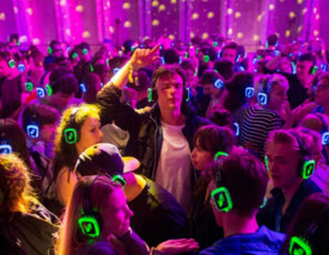 A crowd of people wearing headphones and dancing in a pink-lit room