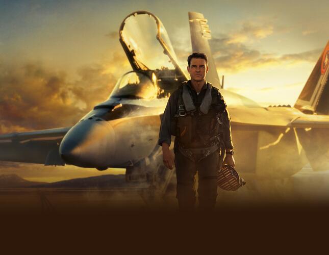 Image is promotional photo for Top Gun film . Tom Cruise is walking towards the camera with a jet in the background.