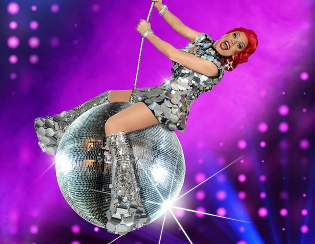 Image shows La Voix in glittery short dress and knee high boots... swinging on a glitter ball!